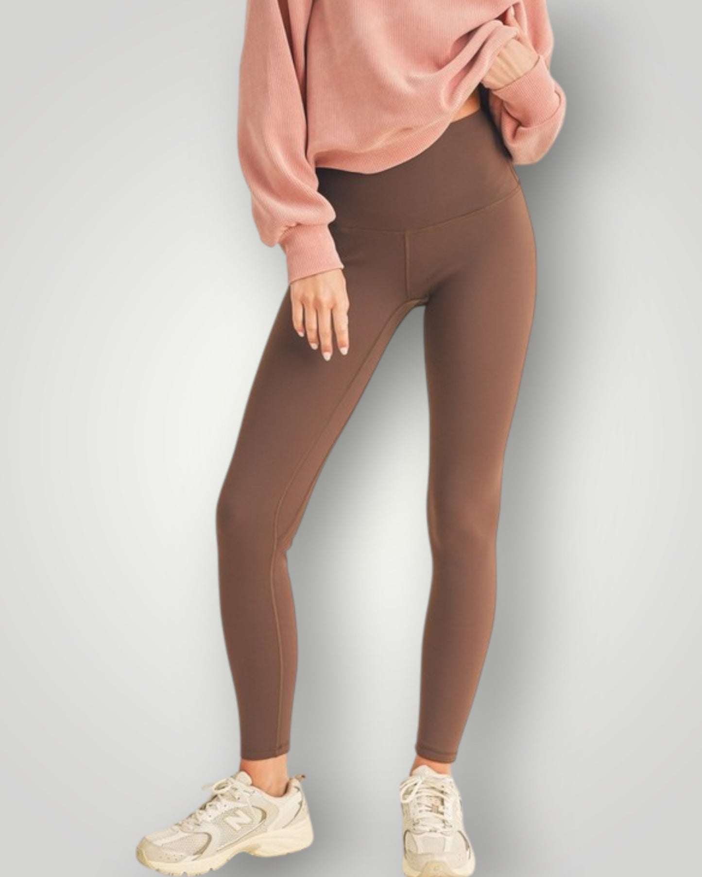 Person wearing brown leggings and a pink sweatshirt on a light gray background