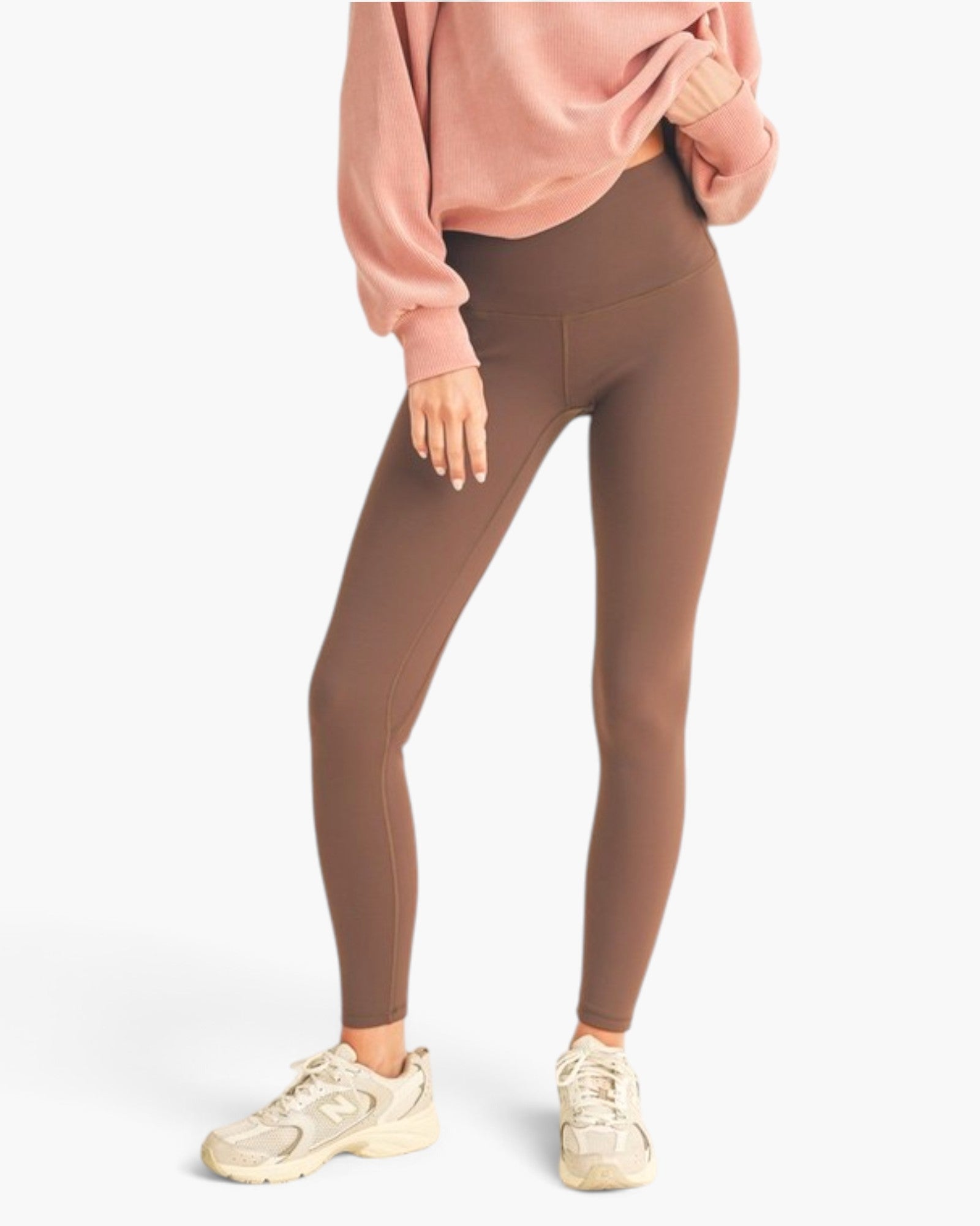A model wearing high-waisted dark gray leggings, a dusty pink sweatshirt, and beige sneakers, shown from the waist down against a clean white background.
