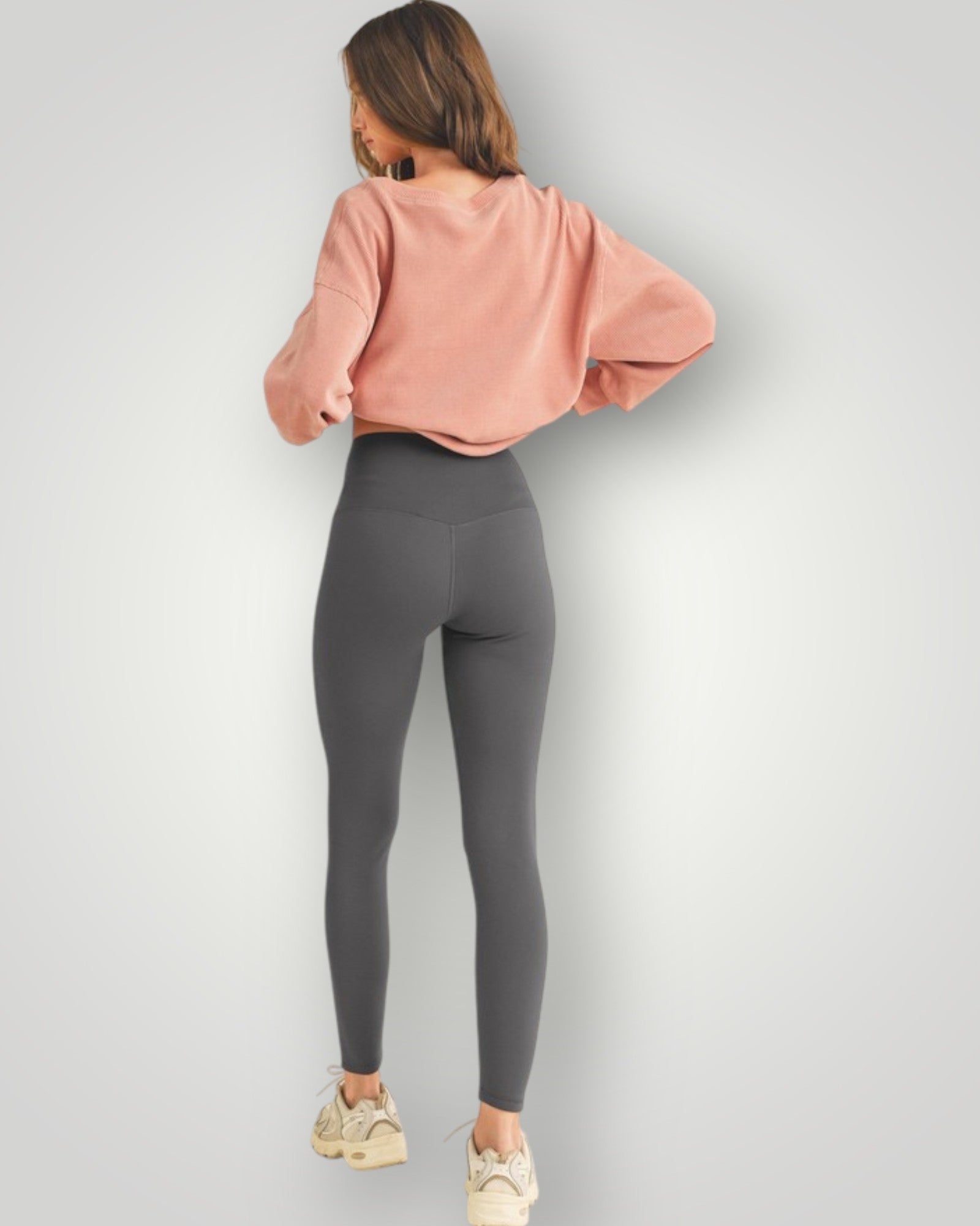 Person wearing a pink sweatshirt and gray leggings on a light gray background