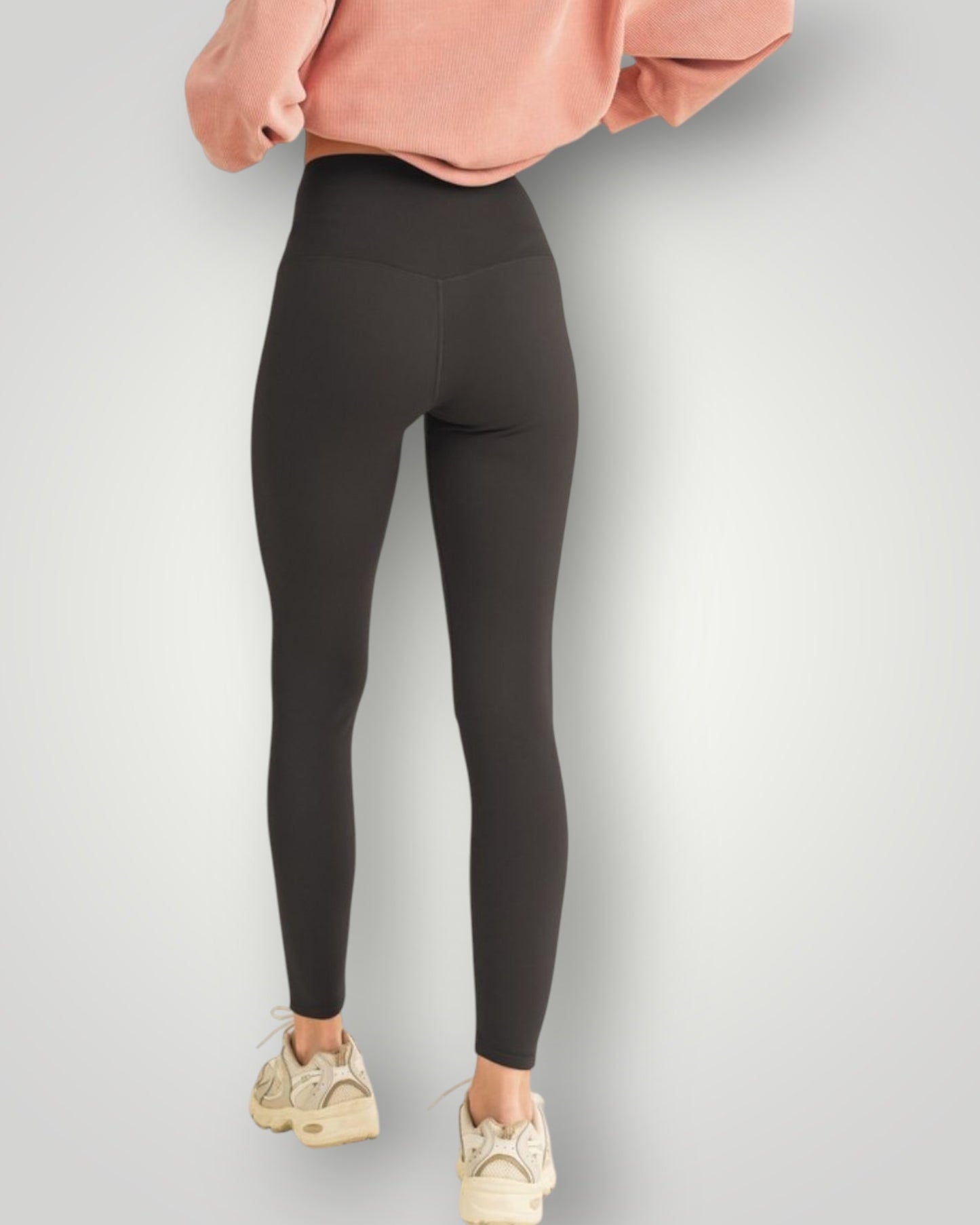Person wearing black leggings and a pink sweatshirt on a light gray background