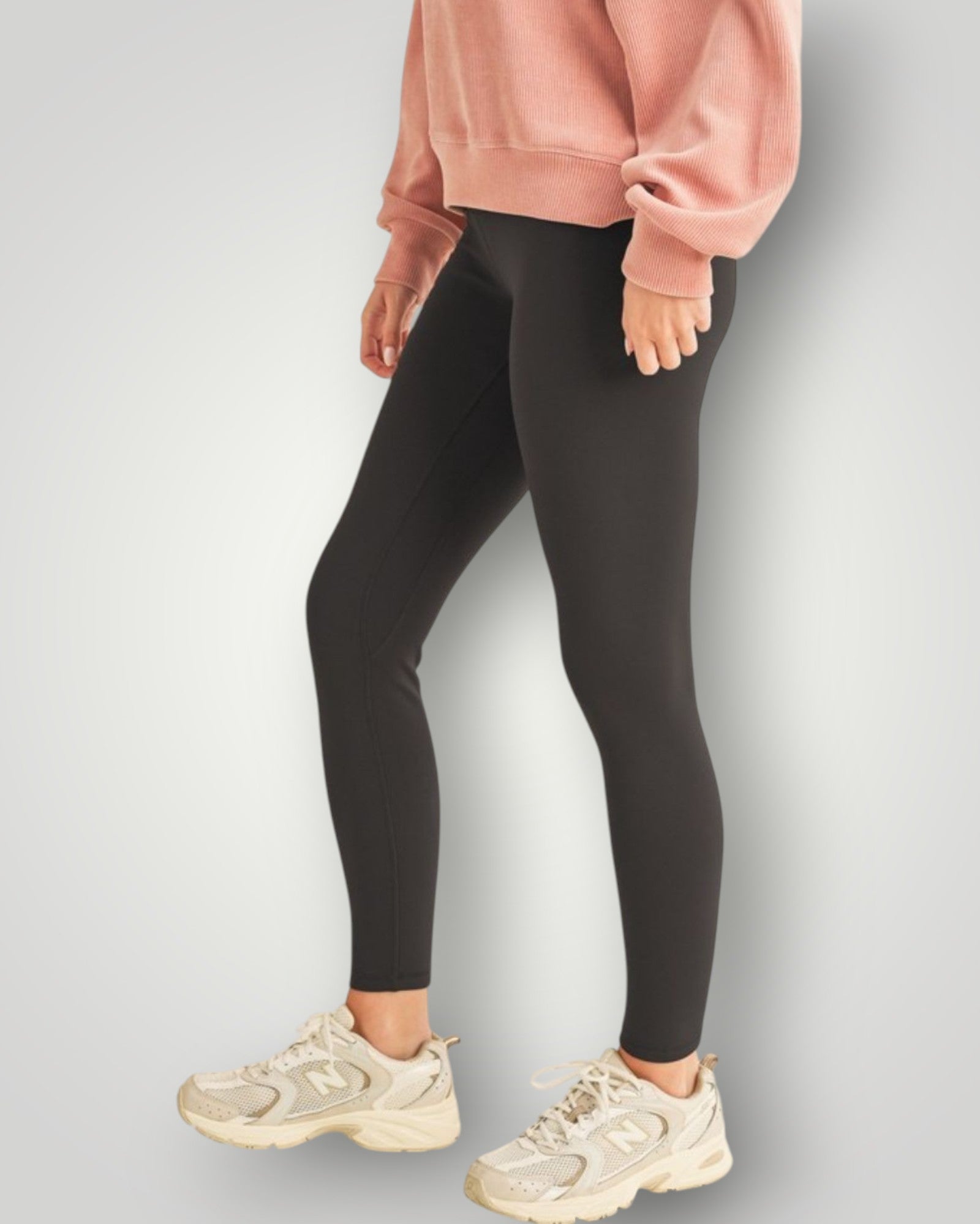Person wearing black leggings and a pink sweatshirt on a light gray background