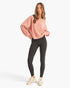 A woman modeling a dusty pink oversized crewneck sweatshirt and black leggings with beige sneakers, standing against a plain white studio background.