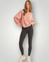 Woman wearing a pink sweatshirt and black leggings on a light gray background