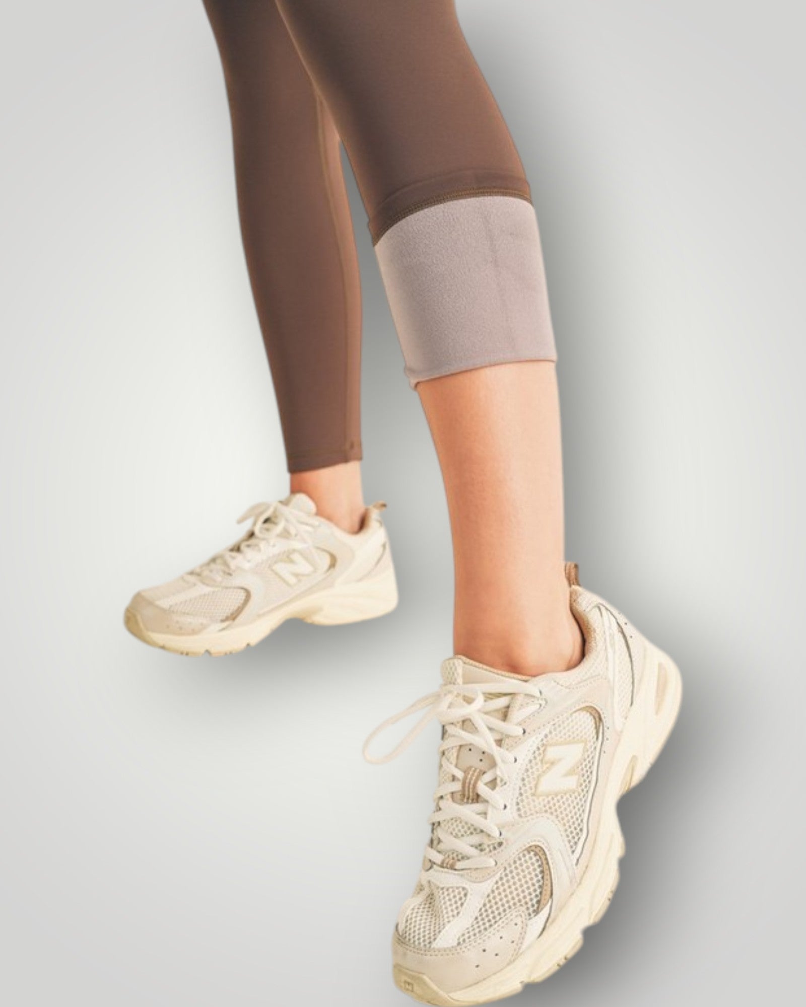 Beige sneakers worn with brown leggings on a light gray background