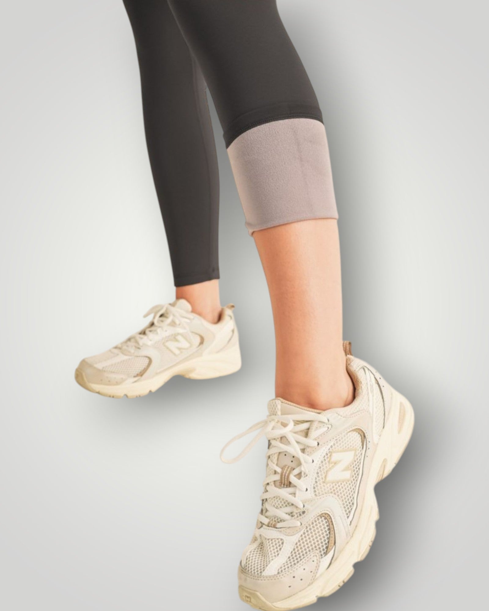 Beige sneakers worn with black leggings on a light gray background