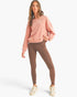 A woman modeling a dusty pink crewneck sweatshirt and brown leggings with white sneakers, standing against a light gray studio background.