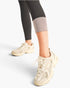 Beige New Balance 9060 sneakers worn with black and gray leggings, shown from the knees down on a light gray studio background.