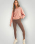Woman wearing a pink sweatshirt and brown leggings on a light gray background