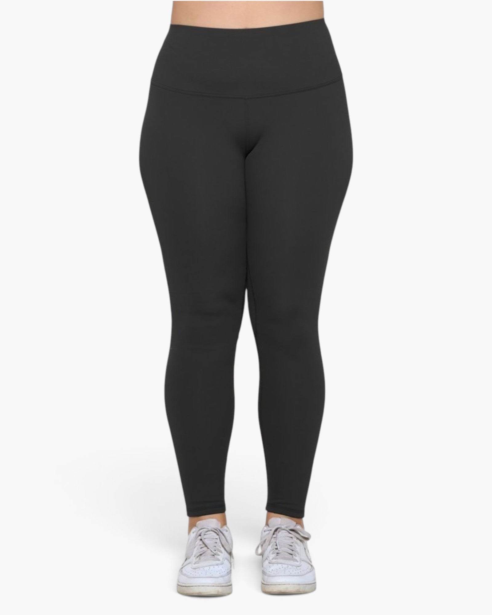 A person wearing high-waisted black leggings and white sneakers, shown from the waist down against a plain light background.
