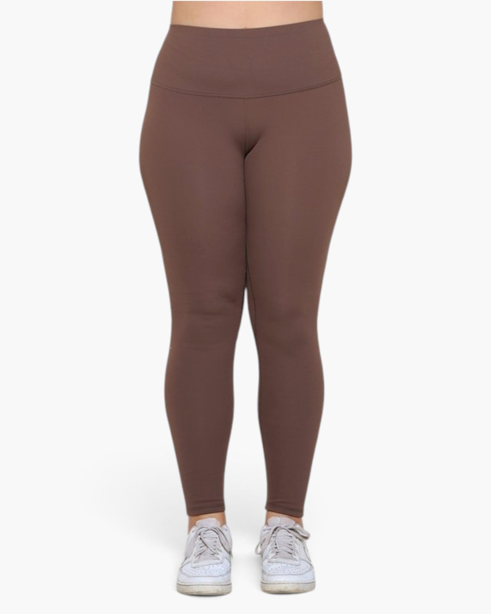 A person wearing high-waisted, full-length leggings in a solid medium brown color, paired with white sneakers, shown from the waist down against a plain white background.