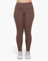 A person wearing high-waisted, full-length leggings in a solid medium brown color, paired with white sneakers, shown from the waist down against a plain white background.