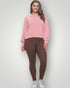 Woman wearing a pink sweatshirt and brown leggings on a white background