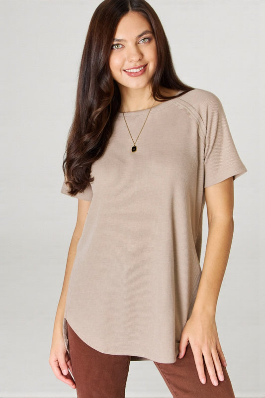 Woman wearing a beige t-shirt and brown pants on a plain background