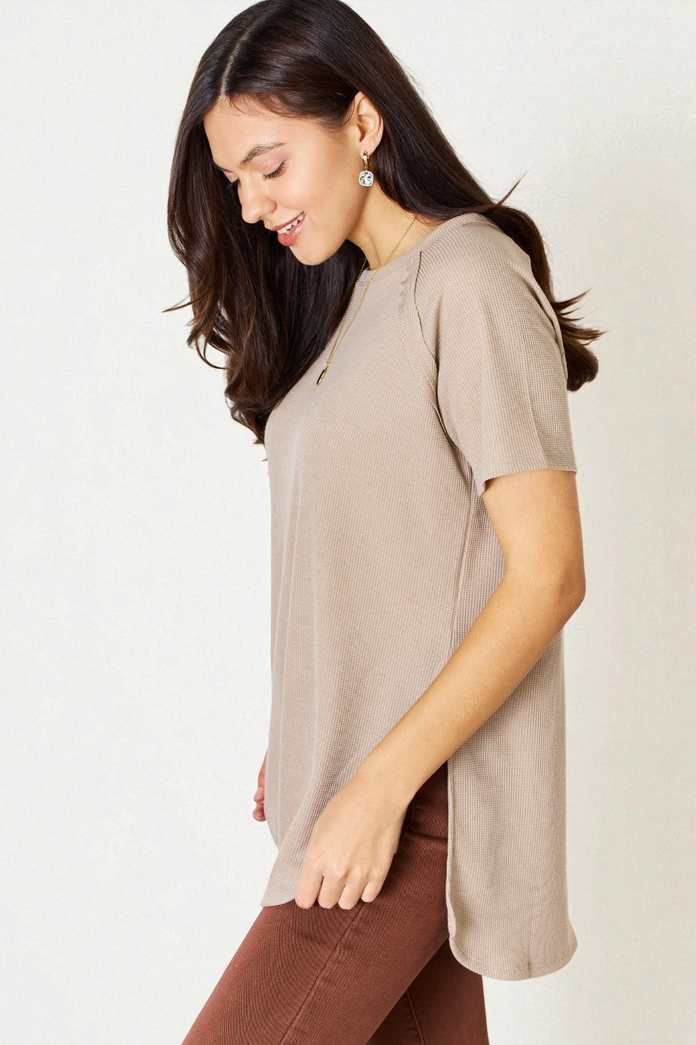 Woman wearing a beige top and brown pants on a white background