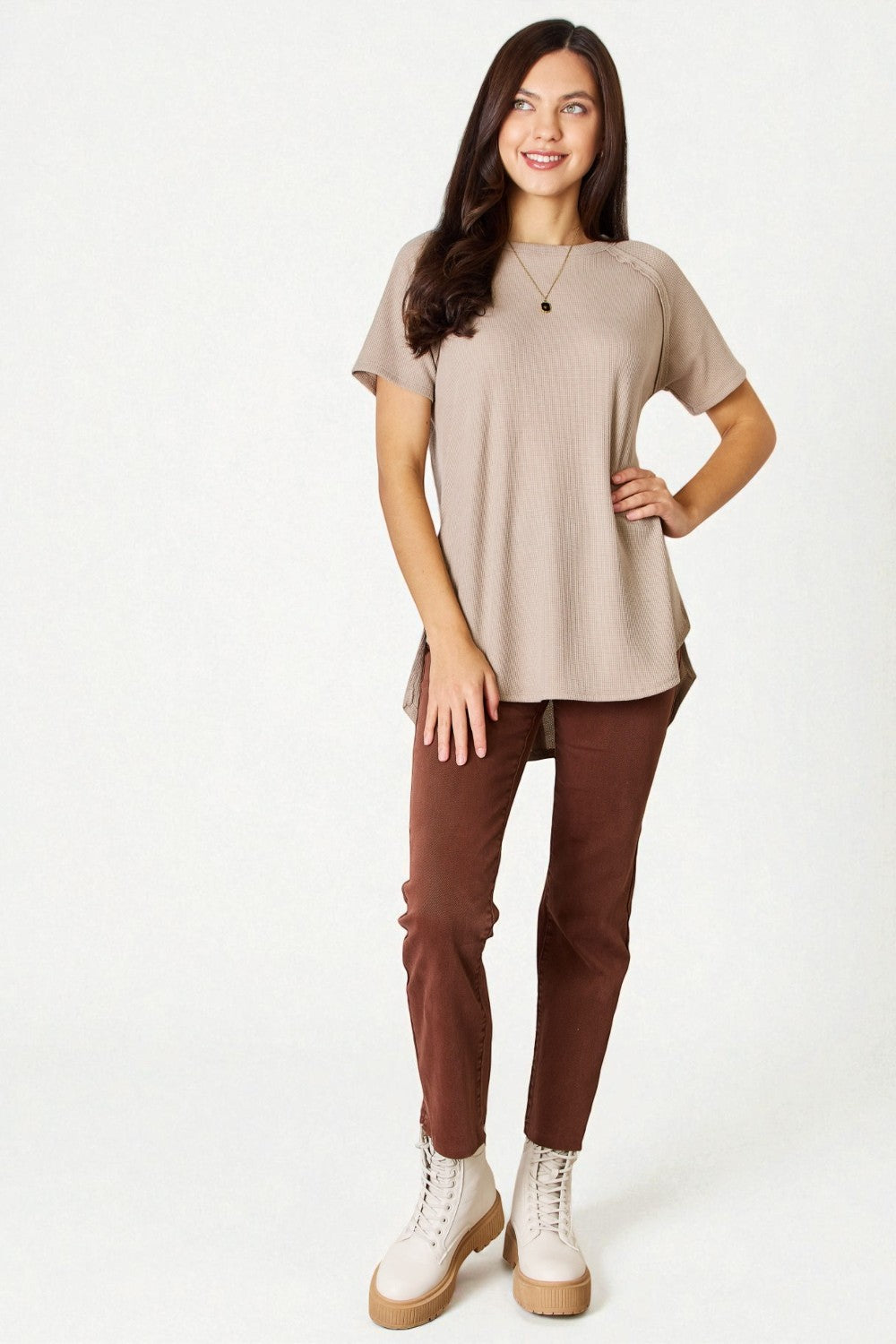 Woman wearing a beige top and brown pants on a white background