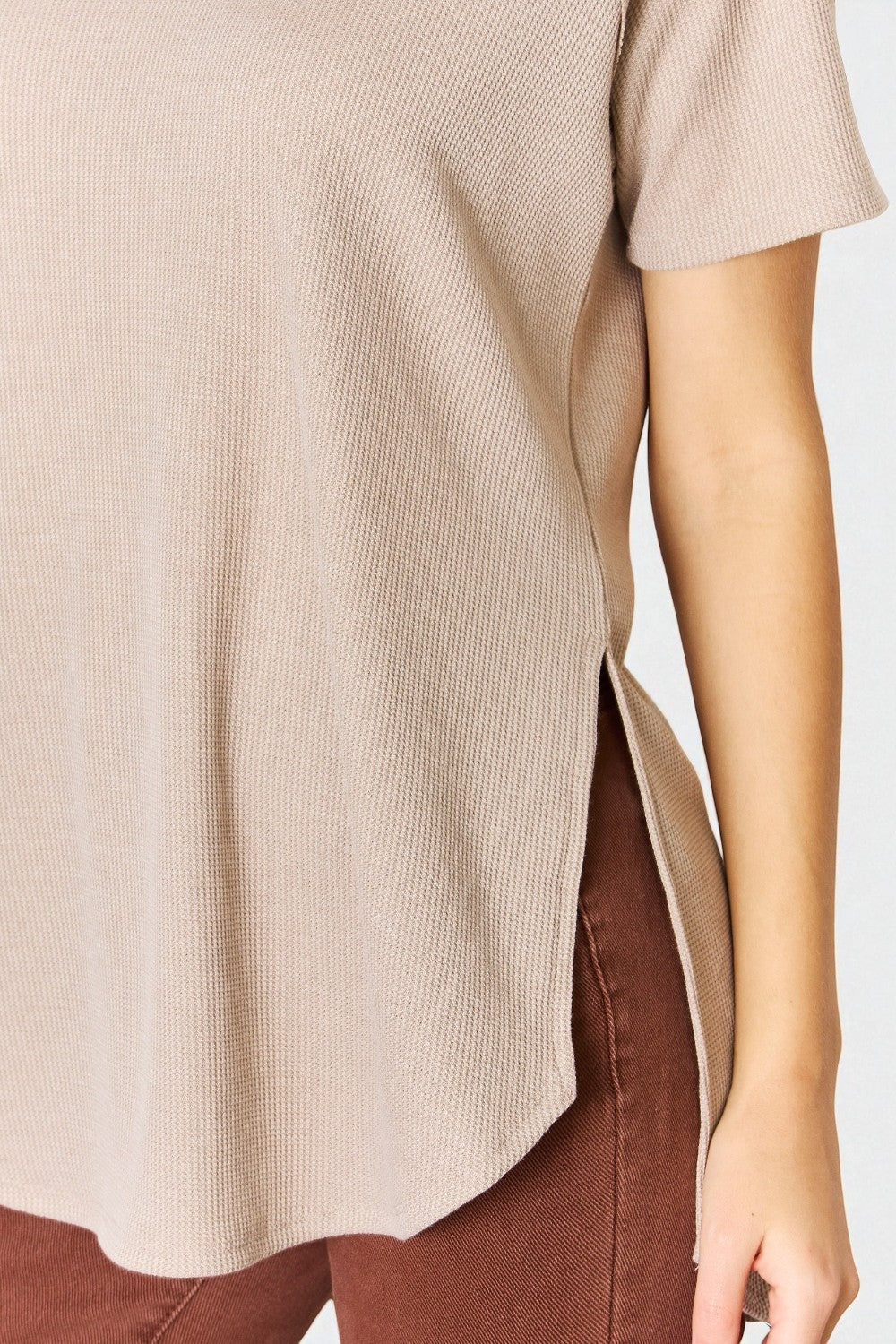 Beige ribbed sweater with a side slit worn by a person on a white background