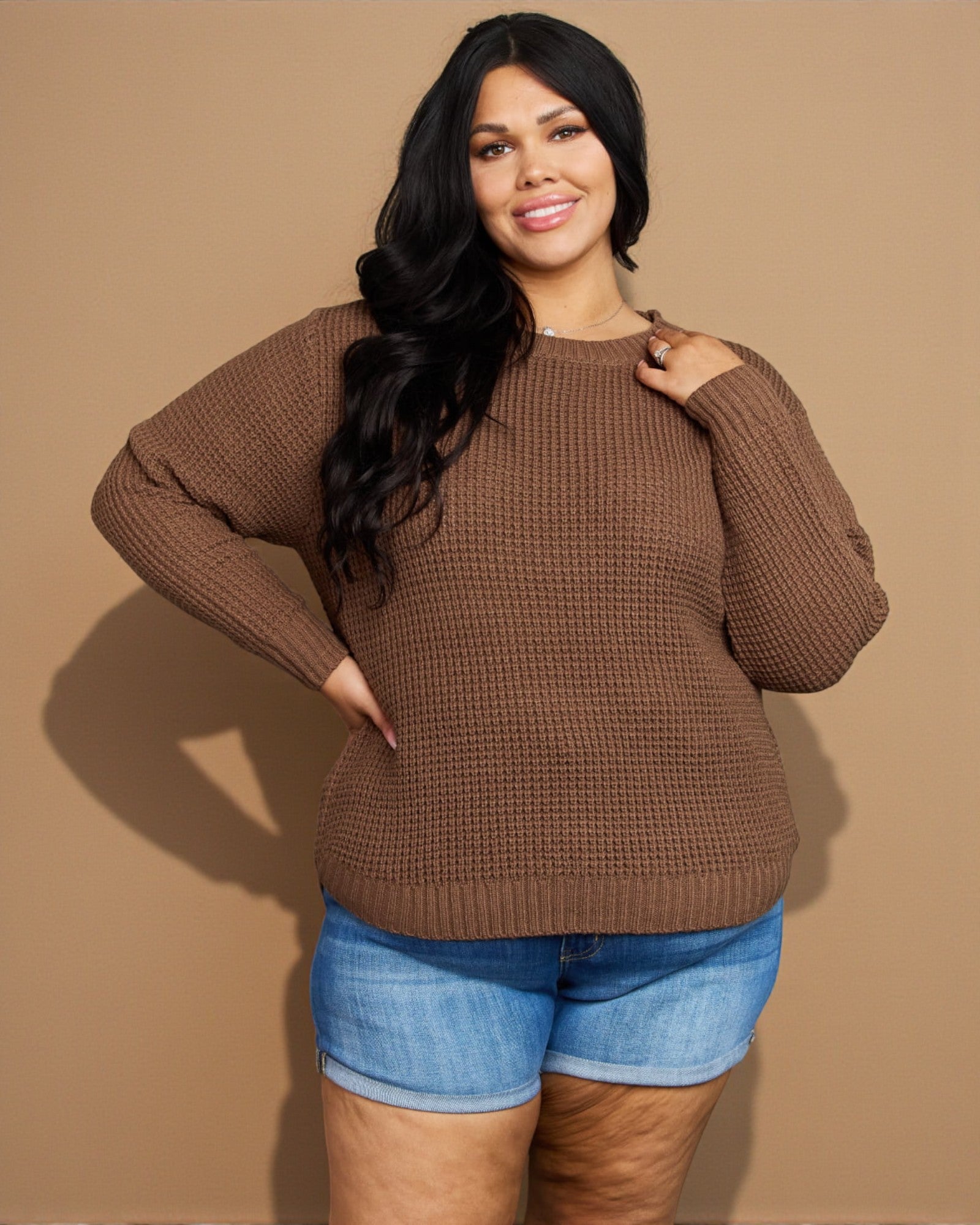 Woman wearing a brown sweater and blue shorts against a beige background