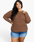 A woman modeling a brown waffle-knit long-sleeve sweater with a crew neck, paired with blue denim shorts, against a plain white background.