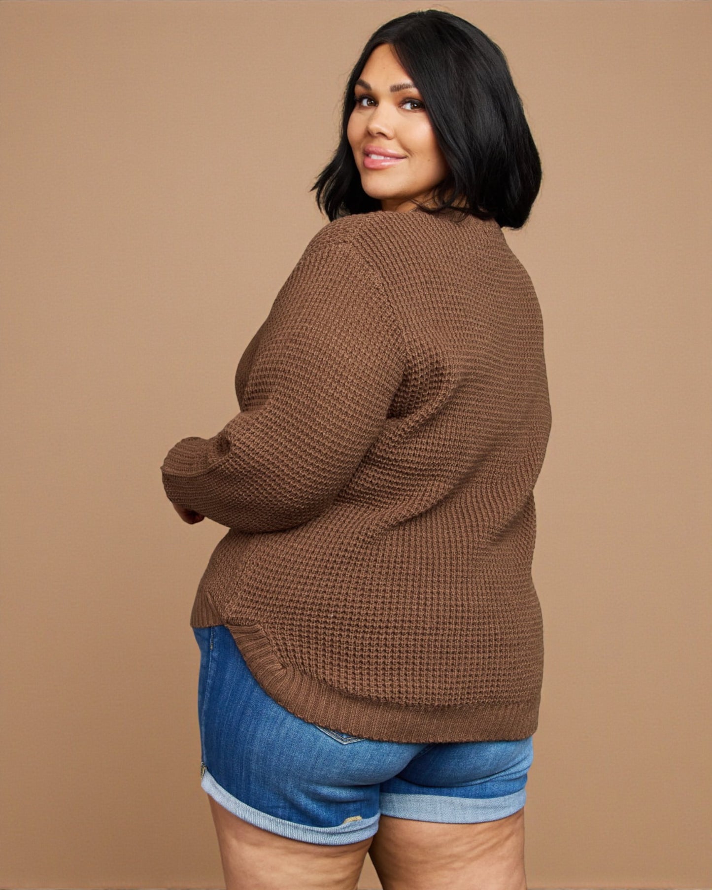 Woman wearing a brown sweater and blue shorts on a beige background