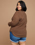 Woman wearing a brown sweater and blue shorts on a beige background