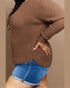 Person wearing a brown knitted sweater and blue shorts on a beige background