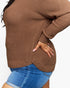 A close-up of a person wearing a brown ribbed knit sweater and blue denim shorts against a plain light background.