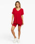 A woman modeling a matching red lounge set consisting of a short-sleeve V-neck top and matching shorts, paired with white sneakers, against a solid white studio background.