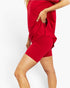 A model wearing a bright red two-piece set consisting of a short-sleeve top and matching fitted shorts, shown from the waist down against a plain white background.