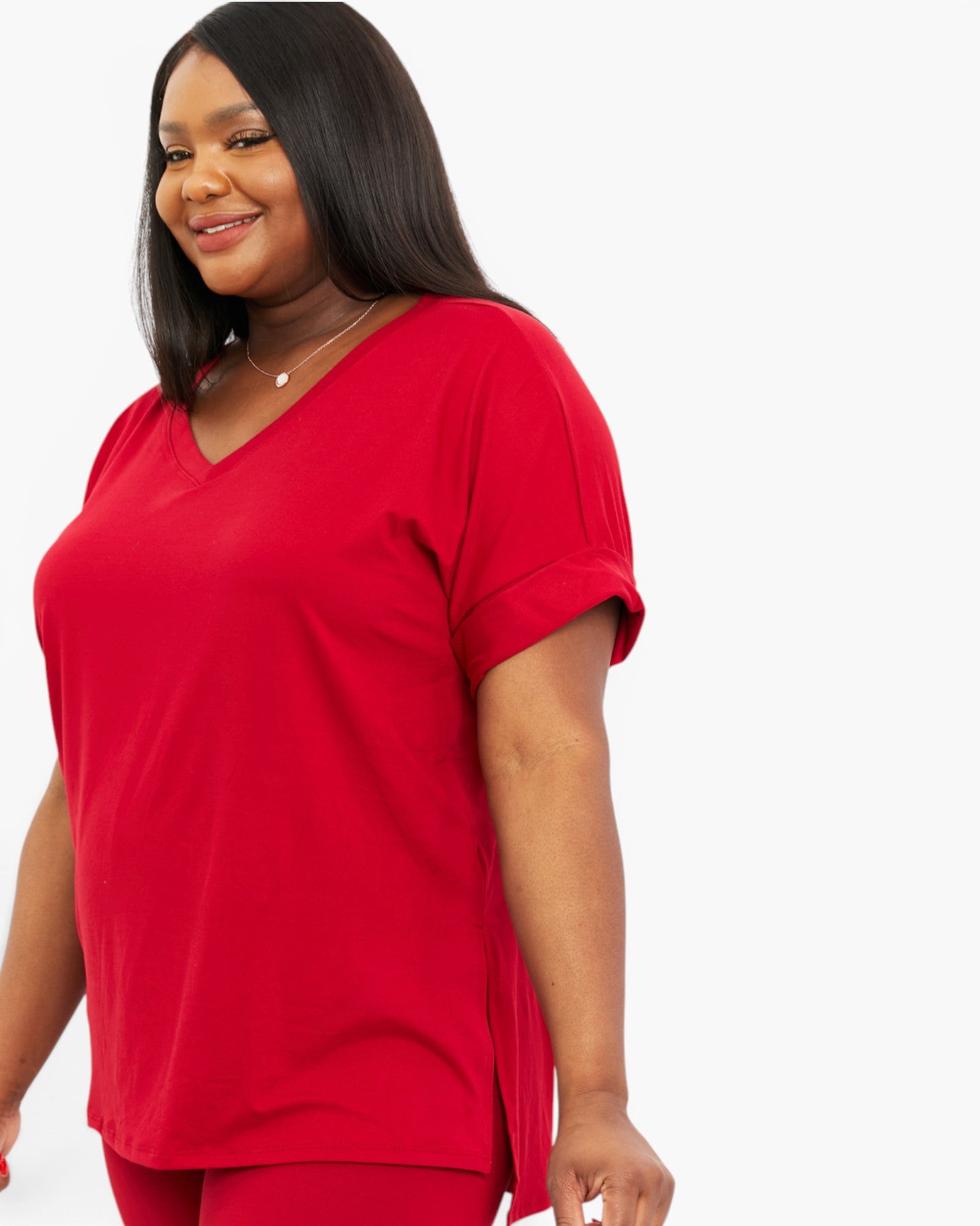 A woman wearing a bright red short-sleeve V-neck top and matching red bottoms, photographed against a plain light gray studio background.