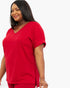 A woman wearing a bright red short-sleeve V-neck top and matching red bottoms, photographed against a plain light gray studio background.