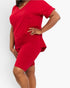 A woman modeling a bright red short-sleeve V-neck mini dress or lounge set against a plain light gray studio background.