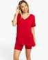 A woman modeling a bright red short-sleeve V-neck lounge set consisting of a loose top and matching fitted shorts, photographed against a clean white studio background.