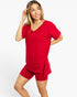 A woman modeling a bright red lounge set consisting of a short-sleeve V-neck top and matching fitted shorts against a plain white studio background.