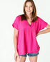 Woman wearing a bright pink blouse and denim shorts on a white background