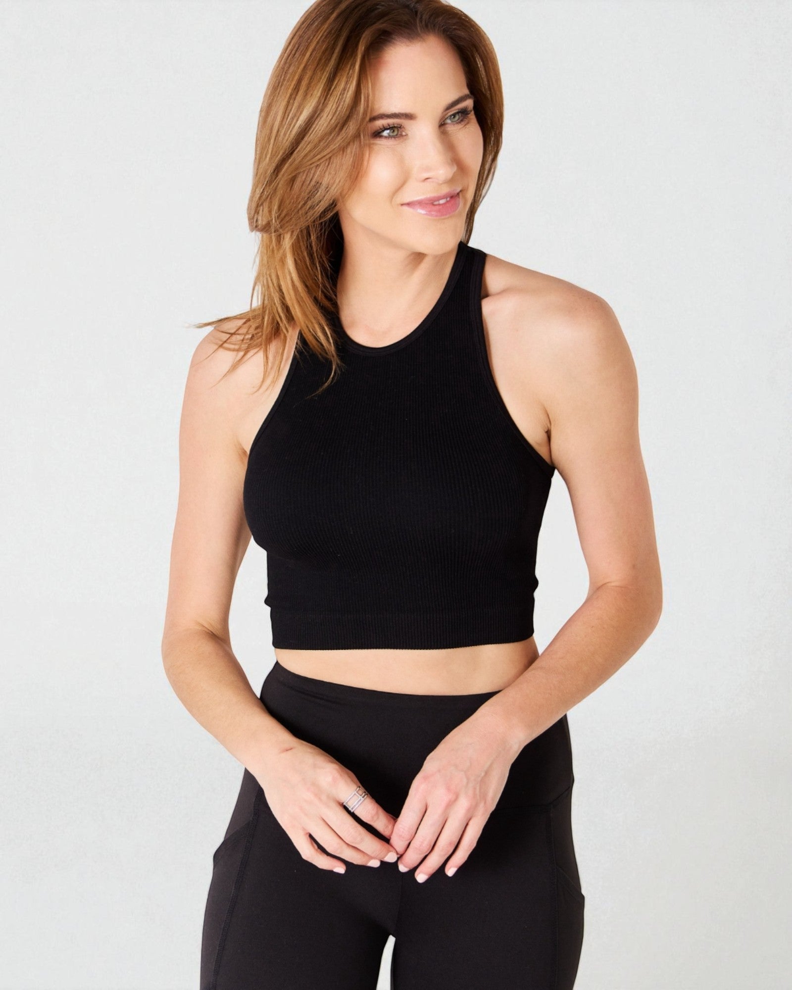 Woman wearing a black crop top and leggings on a light gray background