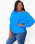 A woman modeling a bright blue, long-sleeve, boat-neck ribbed knit top paired with blue jeans against a plain white studio background.