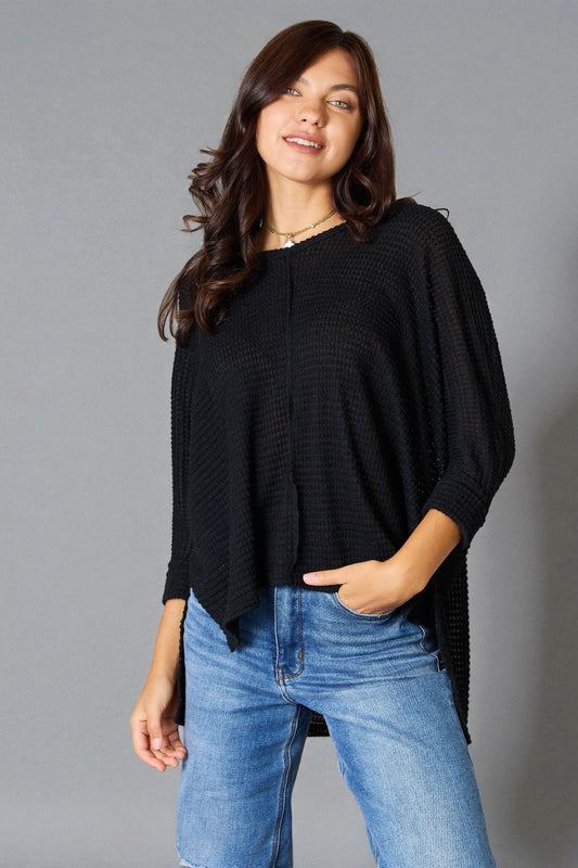Woman wearing a black poncho and blue jeans against a gray background