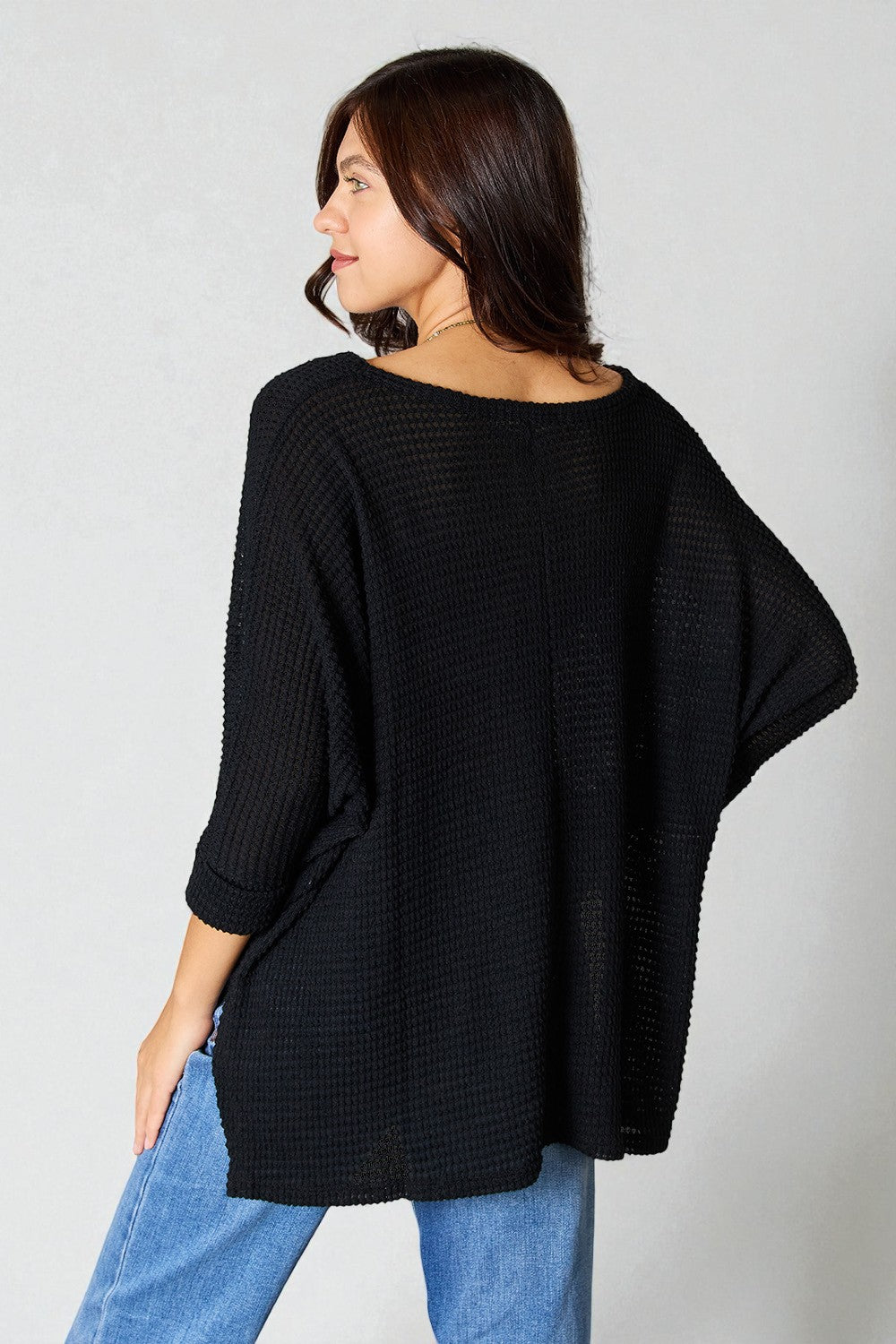 Woman wearing a black oversized sweater and blue jeans against a plain background