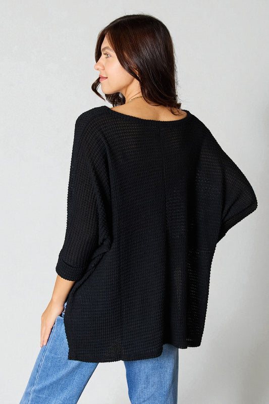 Woman wearing a black oversized sweater and blue jeans against a plain background