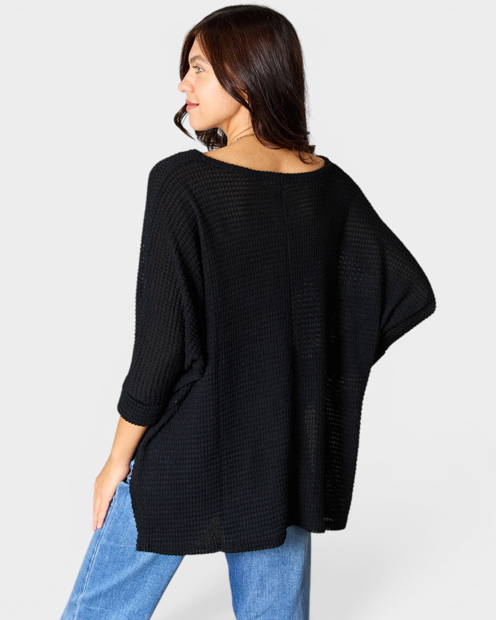 Woman wearing a black oversized sweater and blue jeans on a white background