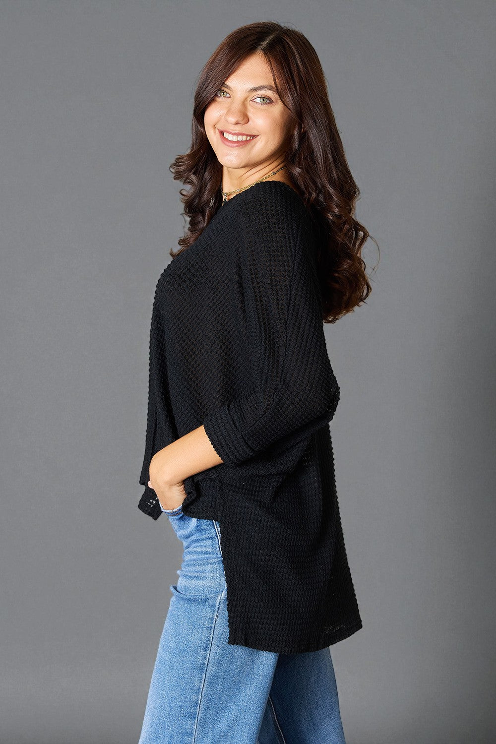 Woman wearing a black sweater and blue jeans against a gray background