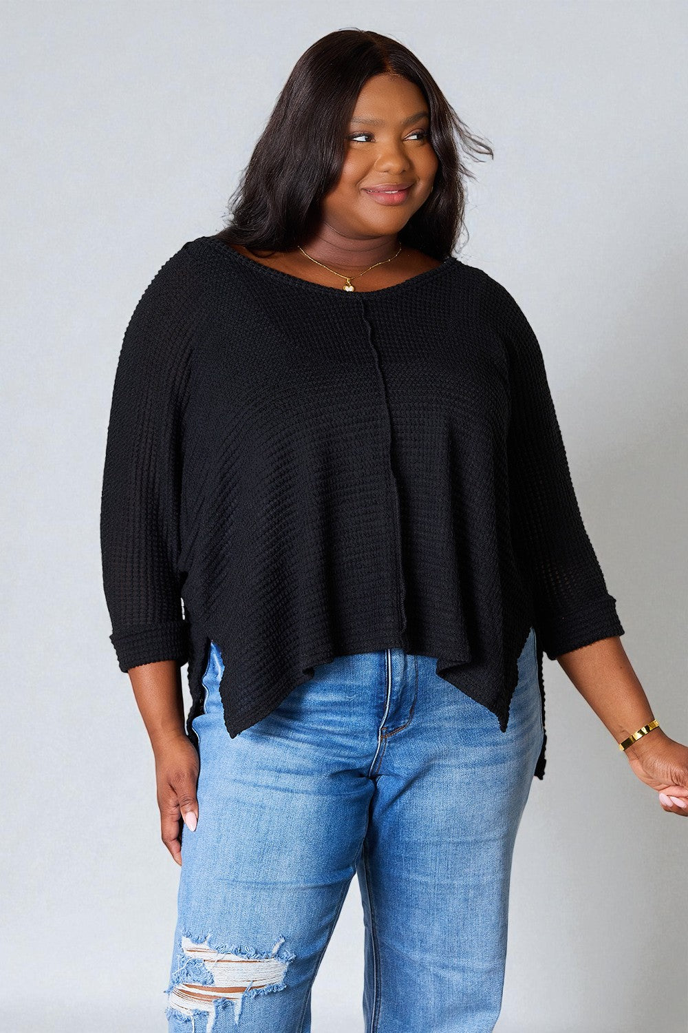 Woman wearing a black sweater and blue jeans against a plain background