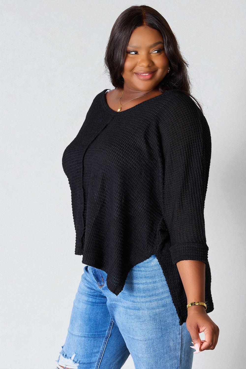 Woman wearing a black sweater and blue jeans against a plain background