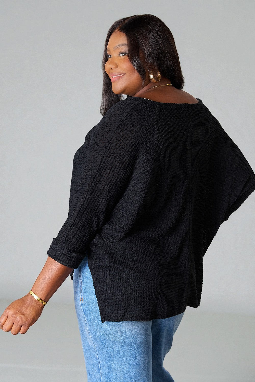 Woman wearing a black sweater and blue jeans against a gray background