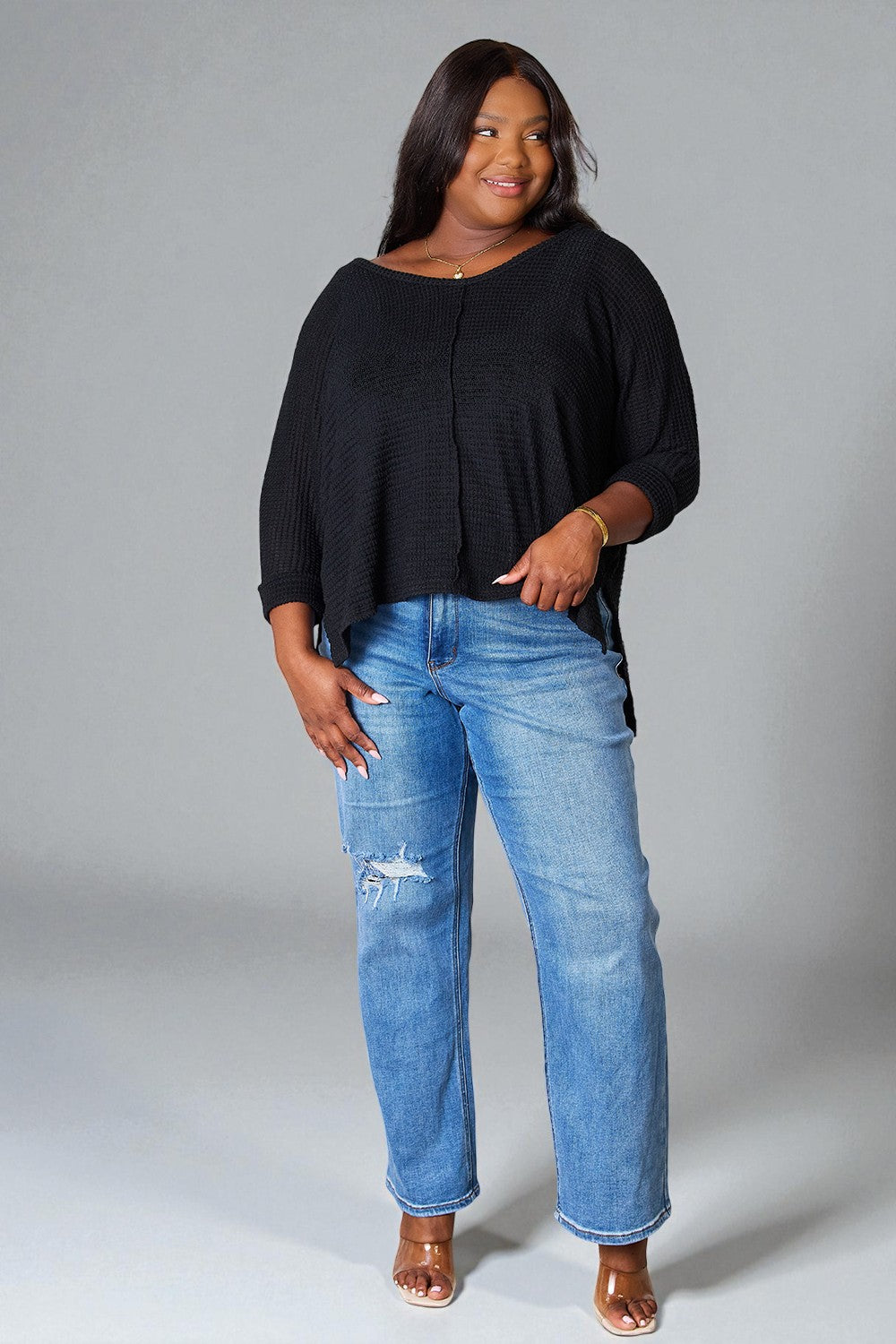 Woman wearing a black top and blue jeans against a gray background