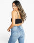 A woman wearing a black ribbed spaghetti-strap tube top and light blue jeans, shown from a rear three-quarter angle against a plain white studio background.