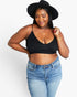 A woman modeling a black ribbed spaghetti-strap crop top with a V-neckline, paired with light-wash blue jeans and a black wide-brim hat, against a plain white studio background.
