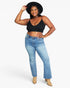 A woman modeling a black spaghetti-strap crop top and light-wash blue flare jeans, styled with a black wide-brim hat and beige ankle boots against a light gray studio background.