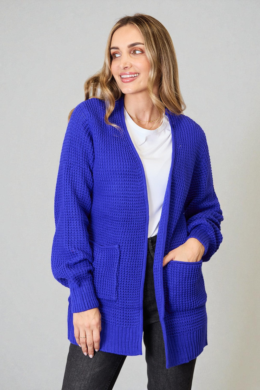 Woman wearing a blue cardigan over a white shirt on a gray background