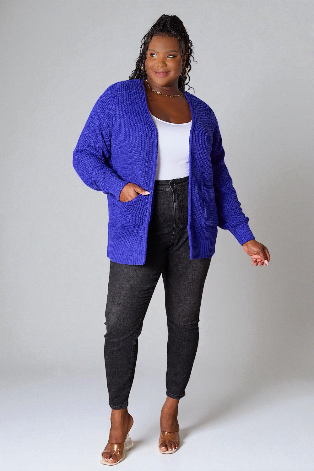 Person wearing a blue cardigan, white top, and black pants on a plain background